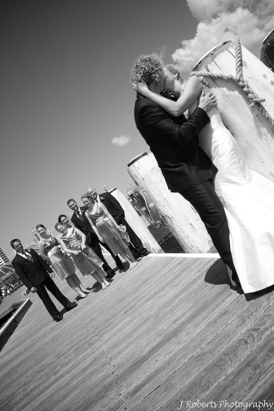 Bride and groom kissing with bridal party looking on - wedding photography